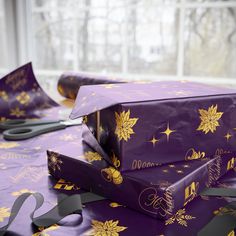 two wrapped presents sitting on top of a purple table cloth with gold stars and snowflakes