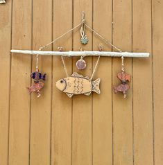 three different colored fish hanging on a wooden wall next to a white stick and some beads