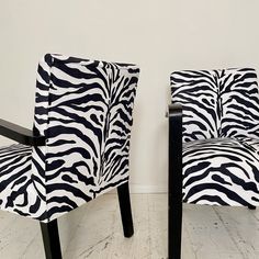 two zebra print chairs sitting next to each other on a hard wood floor in front of a white wall