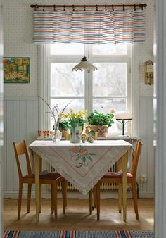 a dining room table with flowers and potted plants on it, in front of a window