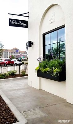 a white building with black windows and plants in the window sill on the sidewalk