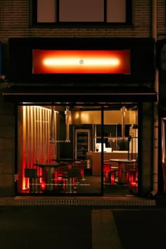 an empty restaurant at night with red lights on the front door and tables set up outside