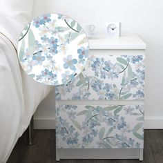 a white nightstand with blue flowers on it and a clock next to the night stand