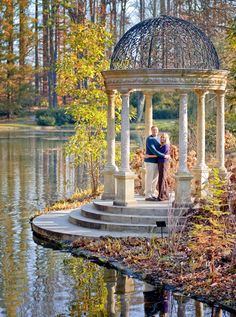 an older couple is posing for a photo in front of a gazebo by the water