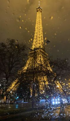 the eiffel tower is lit up at night with rain falling down on it