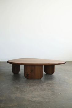 an oval wooden table sitting on top of a cement floor next to a white wall