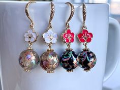 four different colored glass bead earrings hanging from gold earwires on a white cup