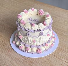 a three tiered cake with pink and purple frosting on a wooden table top