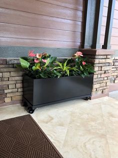 a black planter sitting on top of a floor next to a brick wall with flowers in it