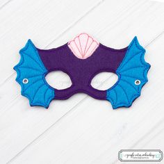 a purple and blue mask on a white wooden background with the words, masquerade