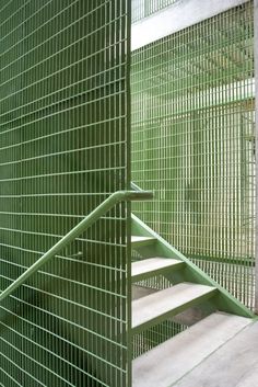 a set of stairs that are next to a green wire mesh wall and concrete floor