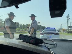 two police officers standing next to each other in front of a car on the road