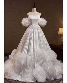 a white wedding dress with ruffled sleeves and flowers on the skirt is sitting on a mannequin