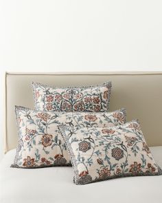 two pillows sitting on top of a bed with white sheets and blue floral print pillow cases