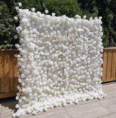 a large white flower covered wall in the middle of a sidewalk with trees behind it