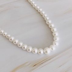 This Pearl Necklace exudes sophistication with a classic design. The pearls are gracefully graduated from small to large to the center, sizes from 4mm to 7mm. Perfect for a timeless staple or to create unique Embellish your neckline with this gorgeous cream-toned pearl necklace! Perfect for daring layering or as a stand-alone statement. Lead and Nickel free Material Composition: Glass pearls, 18k gold-plated brass closure Imported Pearl Necklace Classic, Graduated Pearl Necklace, Queen Liz, Cream Tones, Everyday Dresses, Jewelry Bags, Tops For Leggings, Set Dress, Customized Gifts