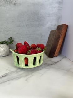 a green bowl filled with strawberries on top of a counter