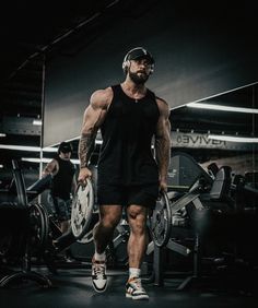 a man in black shirt and shorts with headphones on standing next to gym equipment