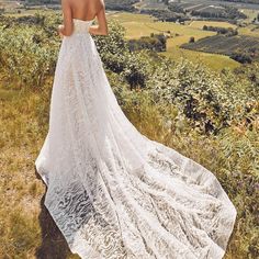 a woman standing on top of a lush green hillside wearing a white dress and hat