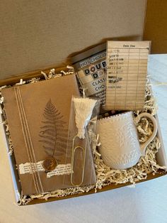 an open box with items inside it on a white tableclothed surface, including a mug and papers