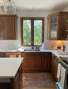 a kitchen with wooden cabinets and white counter tops, along with a window that looks out onto the woods