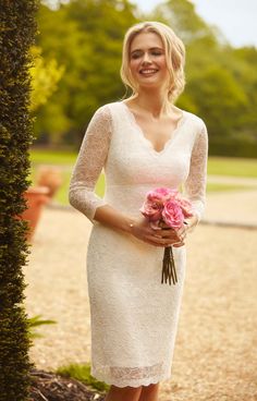 a woman in a white dress holding a bouquet of flowers and smiling at the camera