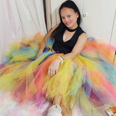 a woman sitting on top of a bed wearing a rainbow colored tulle skirt and white sneakers