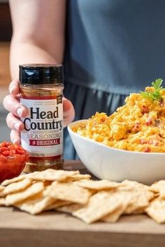 a person holding a jar of head country seasoning next to a bowl of chili and tortilla chips