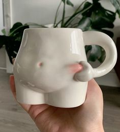 a hand holding a white ceramic elephant mug