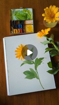 a sunflower painted on a white canvas next to some watercolor paints and flowers