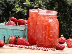 two jars filled with liquid sitting on top of a wooden table next to strawberries