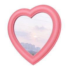 a pink heart shaped mirror hanging from the side of a wall in front of a cityscape