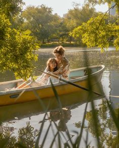 two people in a small yellow boat on the water with trees and grass around them