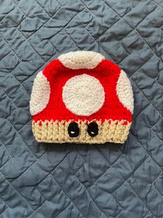 a crocheted mushroom hat sitting on top of a quilted bed cover with black eyes