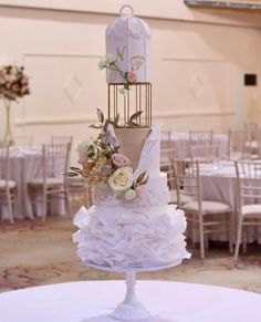 a three tiered wedding cake with birdcage and flowers on top, sitting on a round table