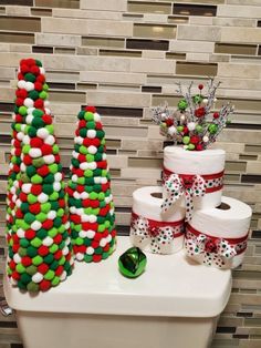 christmas themed toilet paper rolls and candy trees on a bathroom counter with tiled wall behind them