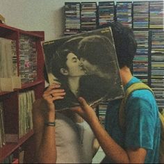 a man holding up a record in front of a book shelf with records on it