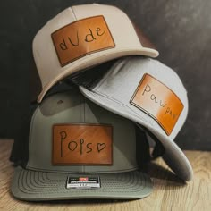 three hats with leather patches on them sitting on top of a wooden table next to each other