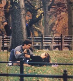 a man sitting on the ground next to a woman laying down in front of a tree