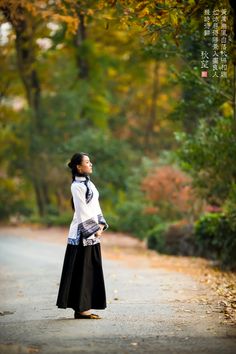 a woman standing on the side of a road with her hands in her pockets and looking up