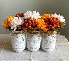 three mason jars with flowers in them sitting on a table