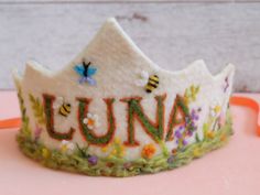 a white crown with the word lunaa written on it and bees flying over it