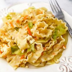 a white plate topped with pasta and veggies next to a knife and fork