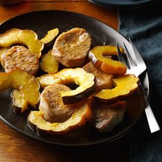 a black plate topped with meat and potatoes on top of a wooden table next to a fork