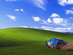 a blue car driving through the grass on a sunny day in front of a green field