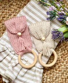 two knitted items sitting on top of a woven basket next to flowers and a wooden ring