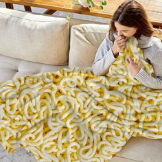 a woman covers her face with a giant blanket made out of yellow rings on a couch