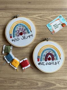 two embroidery hoops with different designs on them sitting on top of a wooden table