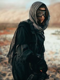 a man with goggles and a hood is standing in the desert looking at something