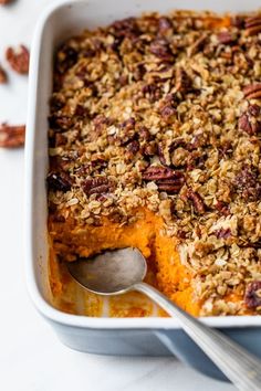 a close up of a casserole dish with pecans on the side and a spoon in it